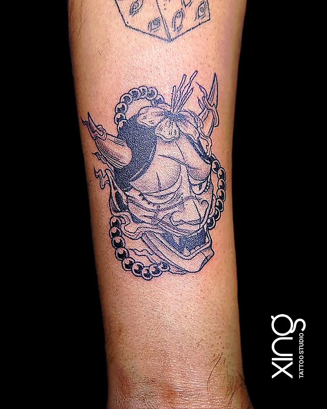 Bold linework demon mask tattoo in progress on forearm