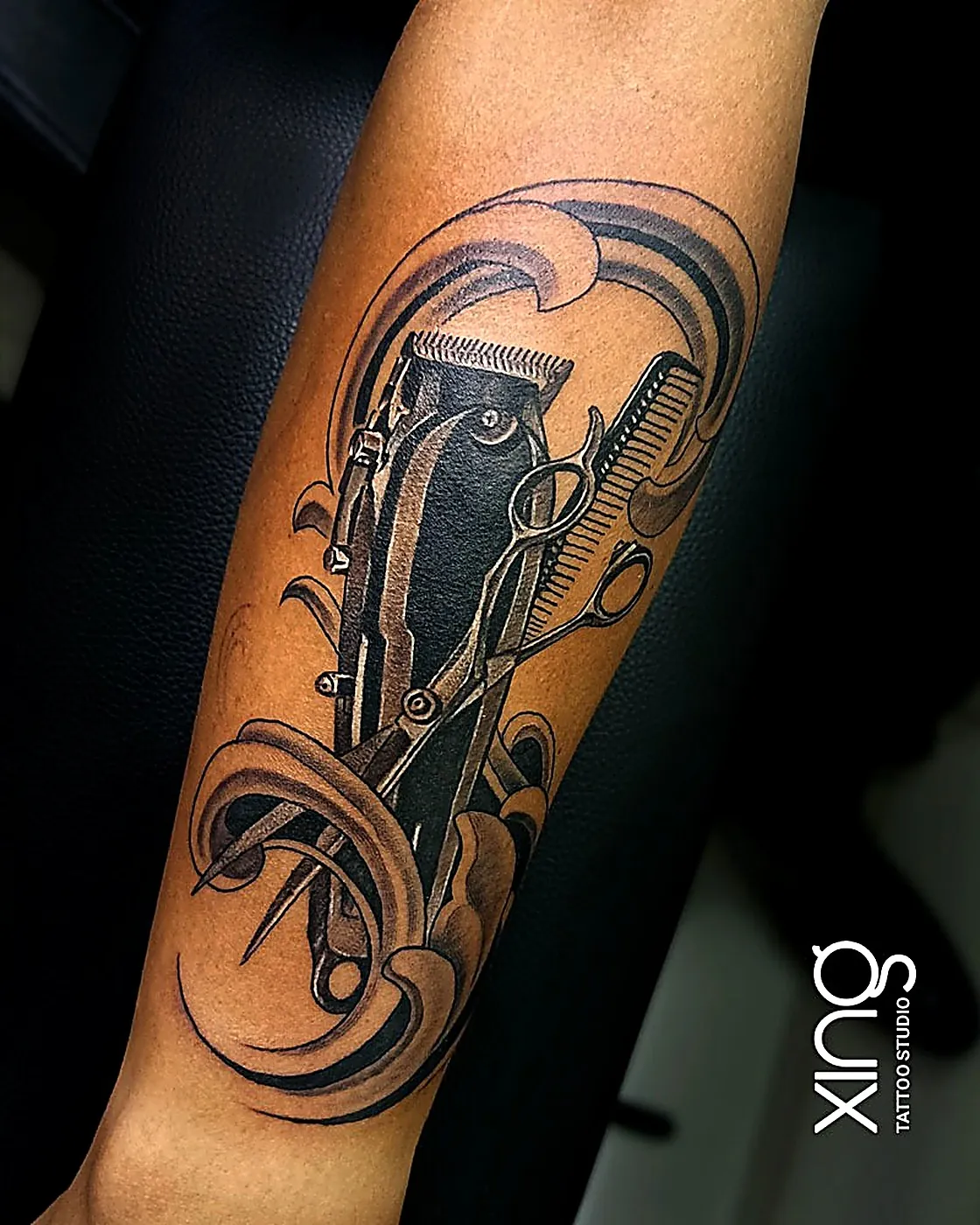 Hyper-realistic barber tools tattoo on forearm showing photographic shading
