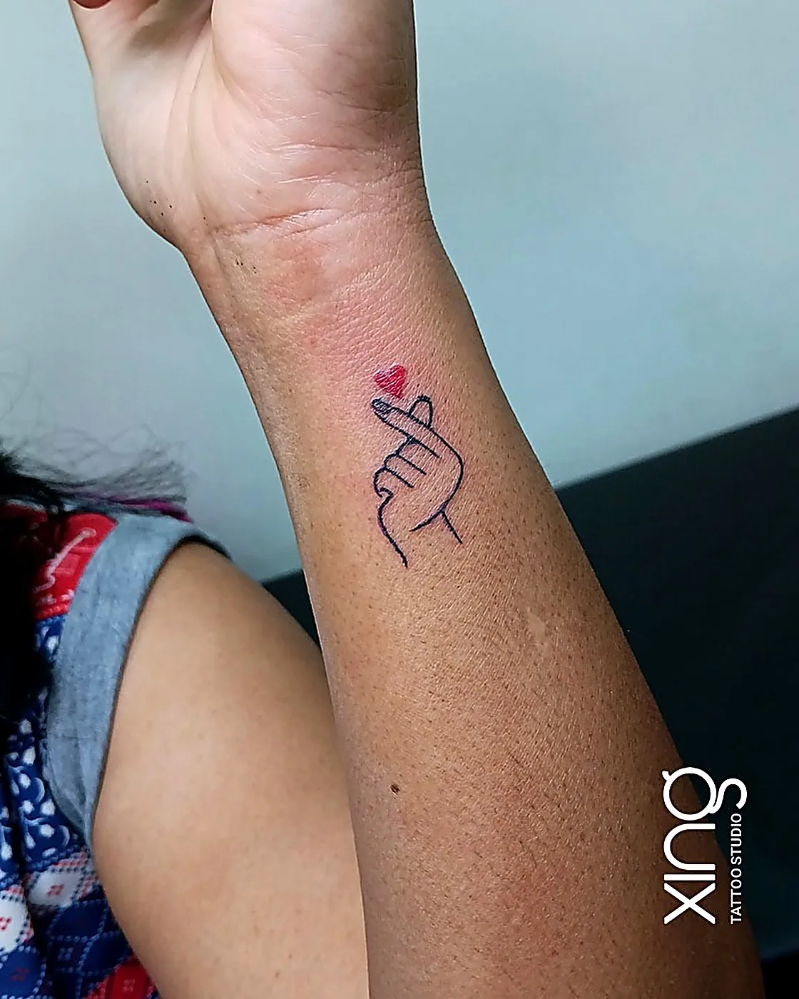 Minimalist finger-heart line tattoo on wrist