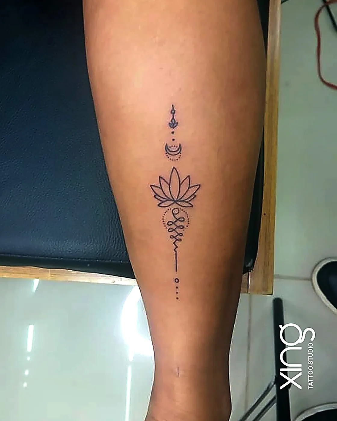 Fine-line lotus and unalome tattoo running down the forearm